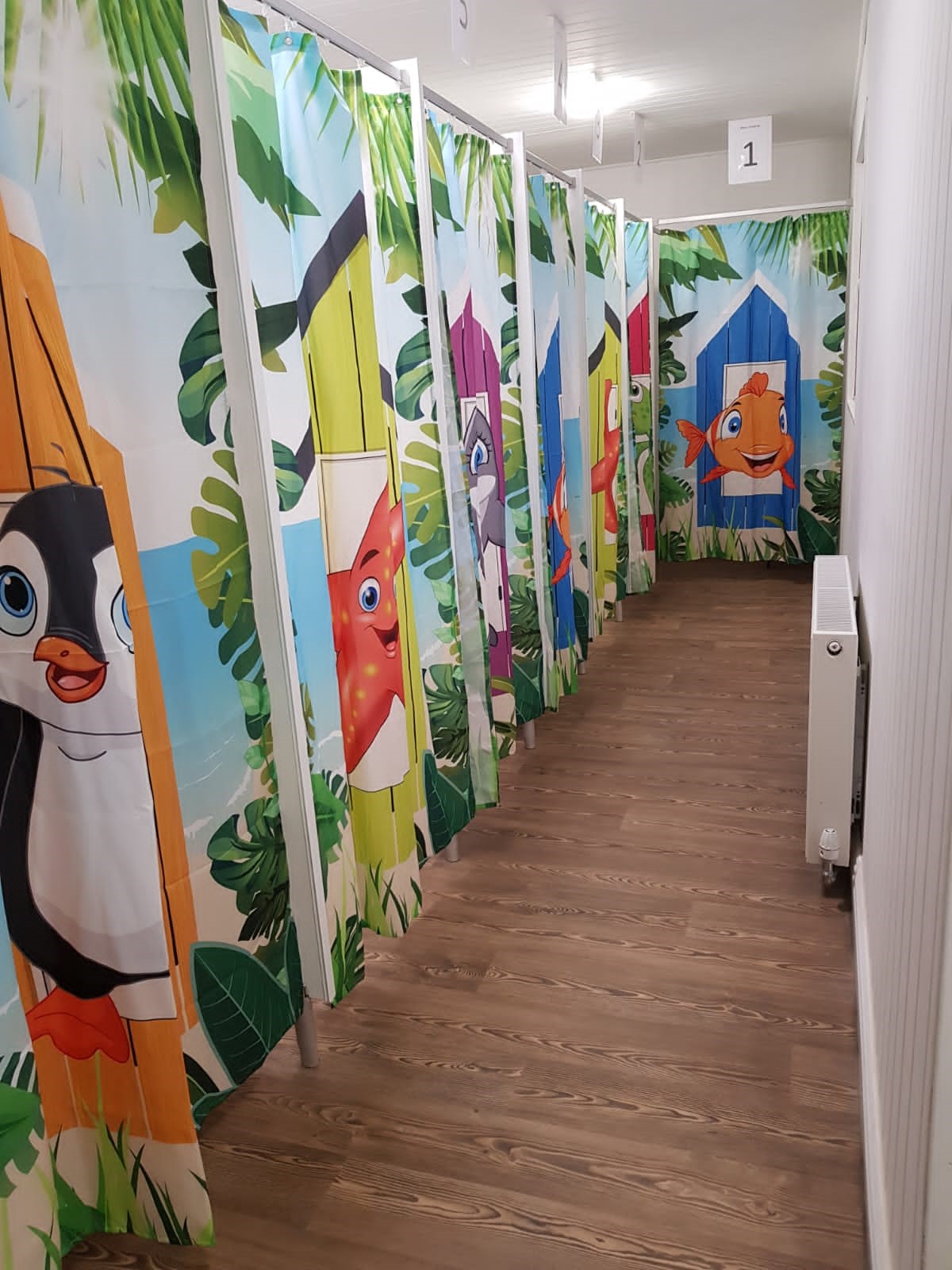 A corridor of individual changing cubicles, each decorated with colourful themed characters from The Little Swim Club