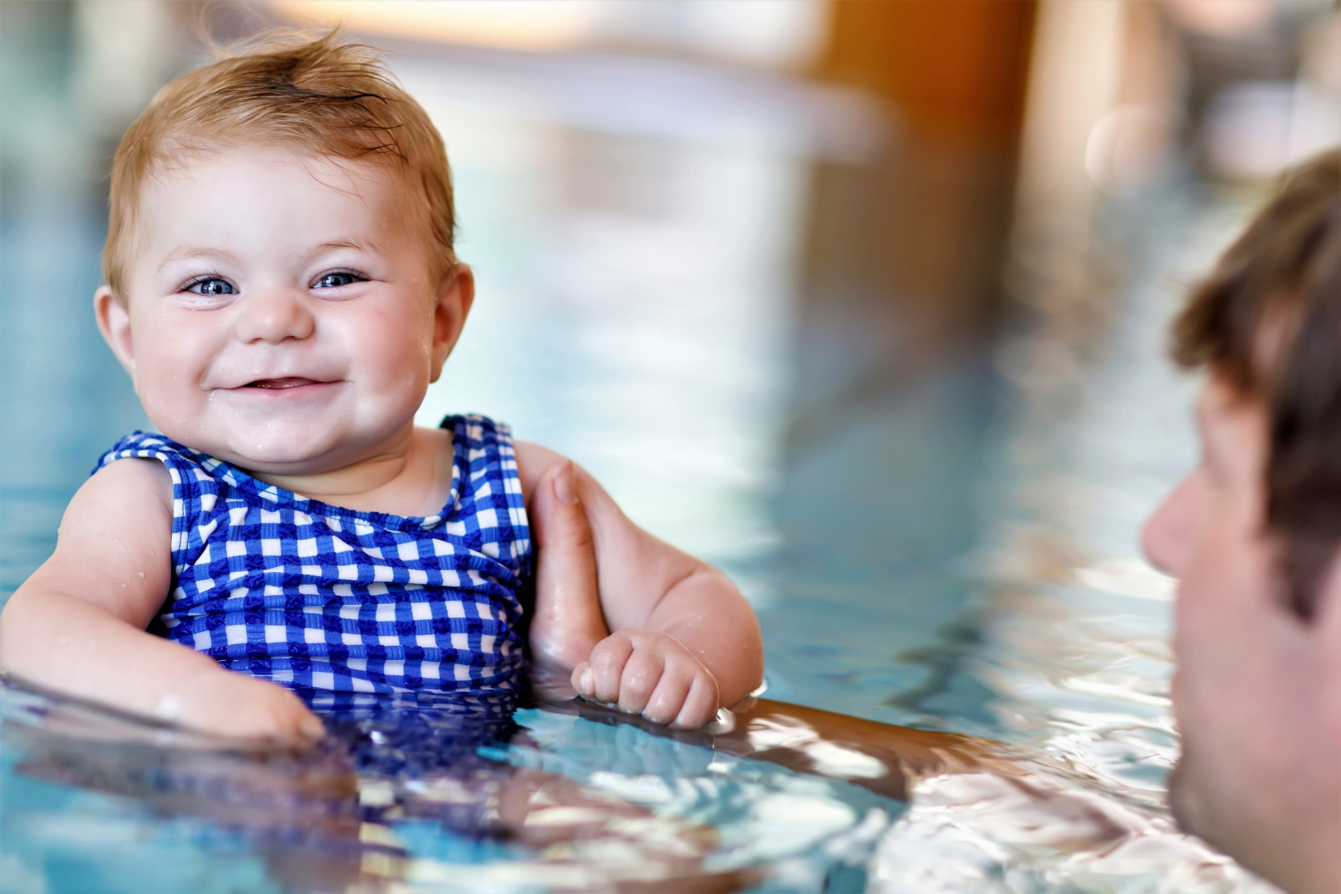 A smiling baby supported in the warm water of the main pool